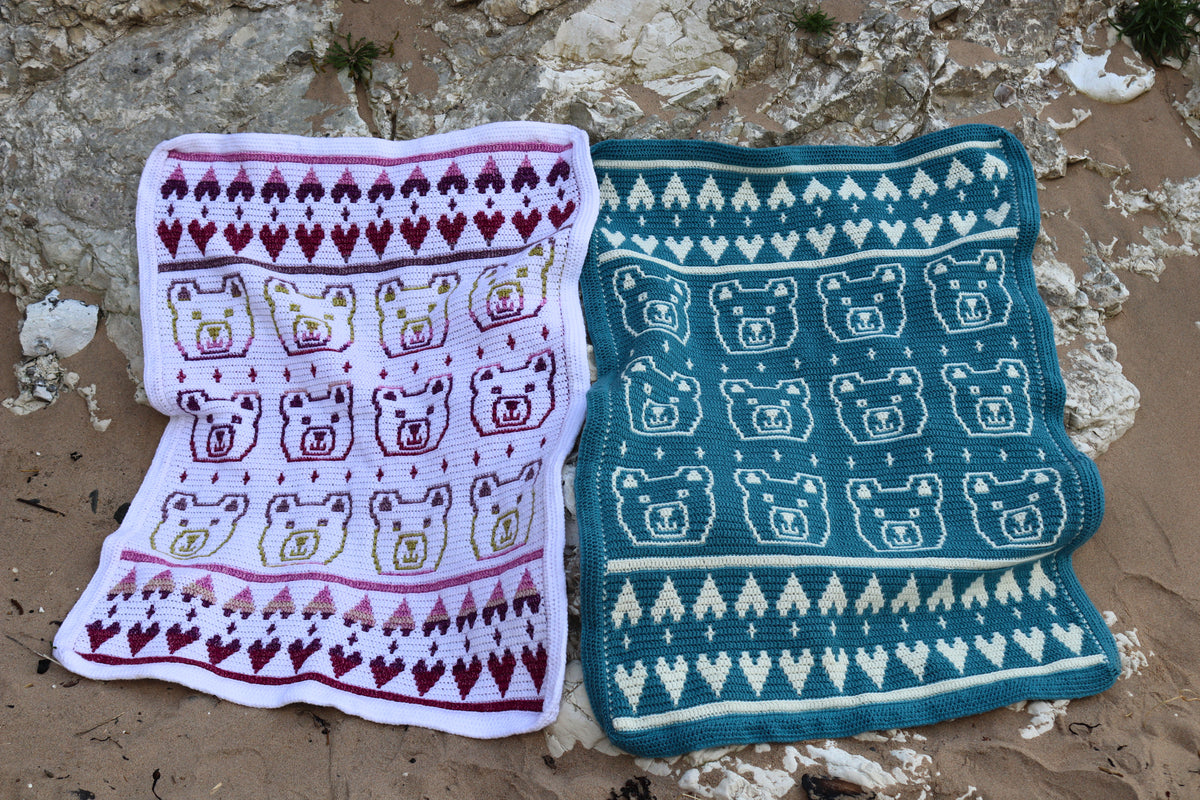 Two knitted baby blankets with bear patterns on a rocky surface